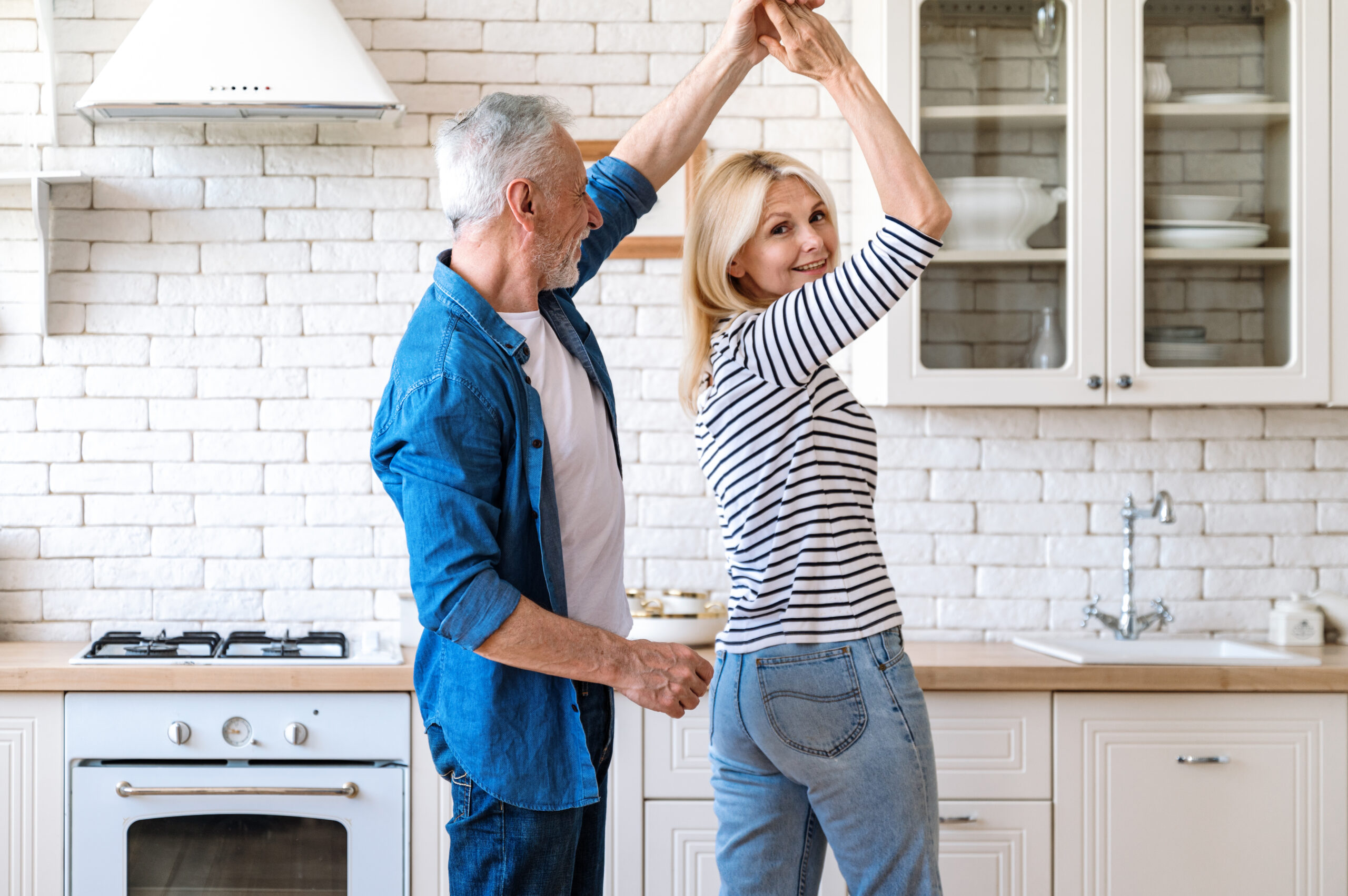 Joyful active mature couple dancing and smiling in kitchen